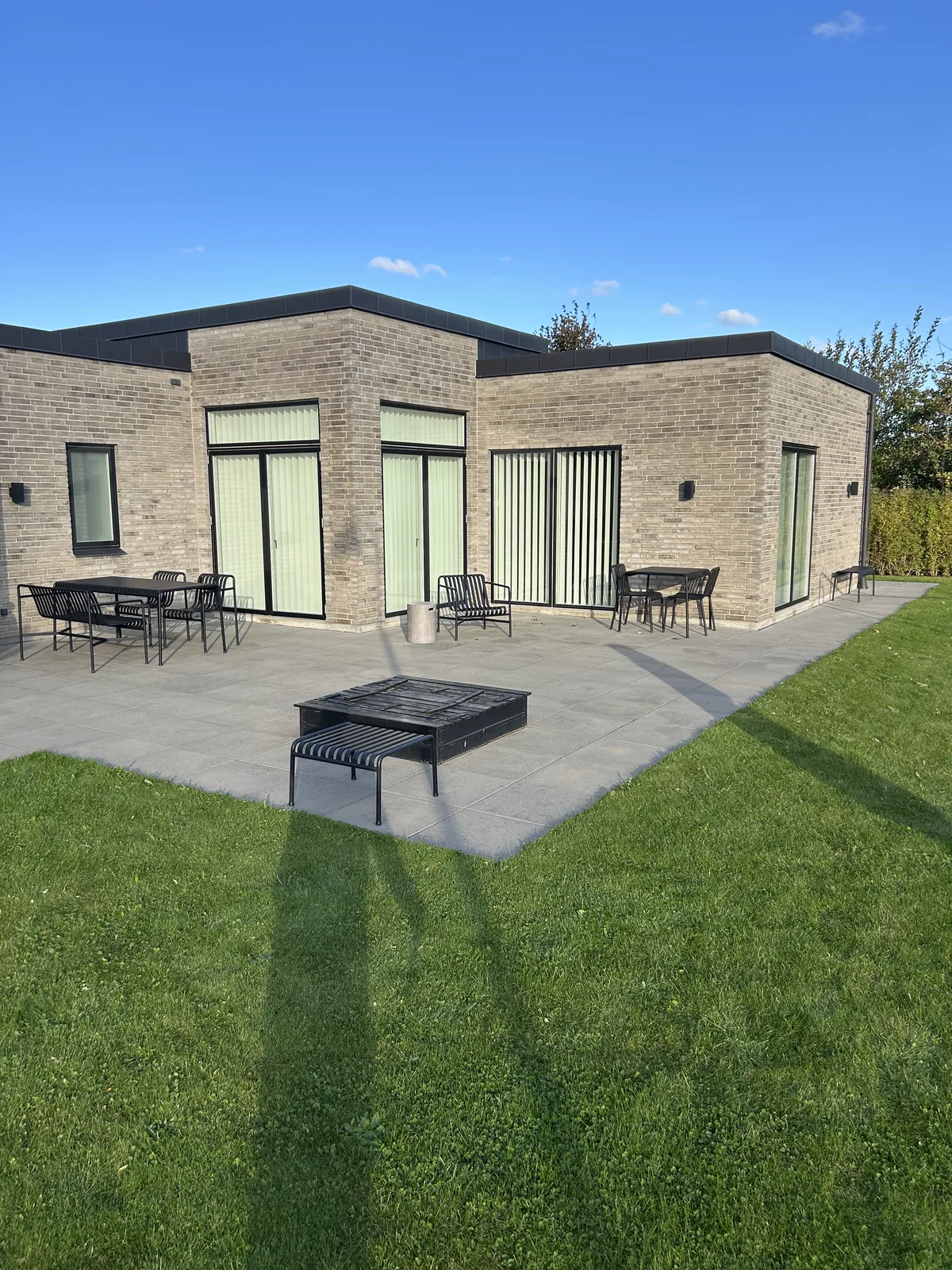 Færdig betonterrasse med havemøbler og bålsted ved moderne muret hus